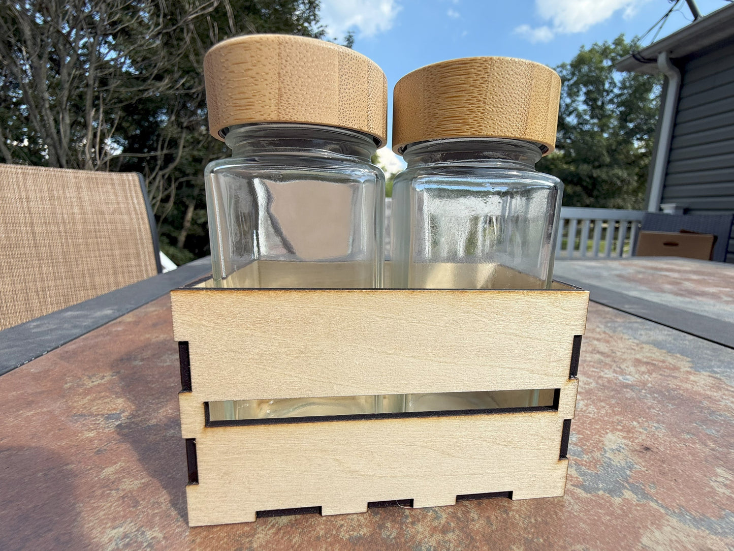 Two glass shaker bottles with bamboo lids in wooden crate